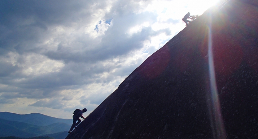 two people ascend up a sloped rock